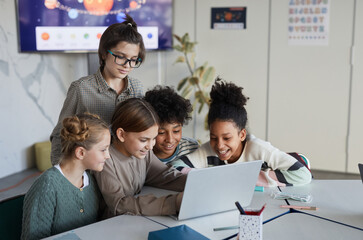 Diverse group of children using laptop together at table in modern school, copy space