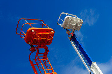 Lift platform with bucket and cherry picker aerial work platforms, construction hydraulic telescopic cranes of orange and white colors, heavy industry, white clouds and blue sky on background