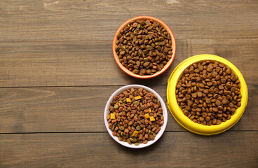 Dry food in pet bowls on wooden background, flat lay. Space for text