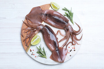 Fresh raw squids with lime and rosemary on white wooden table, top view