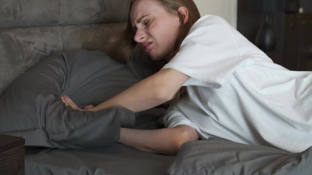 Young woman at home in the bedroom, lying in bed, unable to sleep due to an uncomfortable pillow, suffering from insomnia