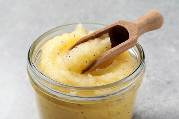 Body scrub with scoop in glass jar on light grey background, closeup