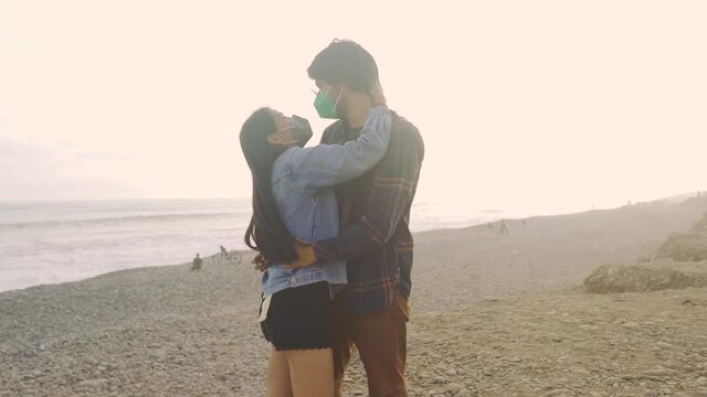Joven pareja latina de novios enamorados caminando durante un hermoso atardecer en la playa. Personas caminando con mascarillas. Romance en tiempos de pandemia 