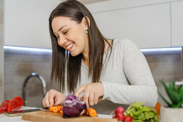 Side view of caucasian woman cutting carrot on the wooden board in the kitchen preparing vegan or vegetarian meal cooking vegetables at home smiling with copy space