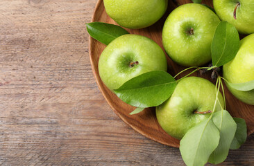 Fresh ripe green apples and leaves with plate on wooden table, top view. Space for text