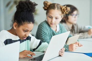 Diverse group of children sitting in row at school classroom and using laptops