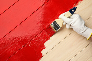 Worker in gloves painting wooden surface with red dye, top view. Space for text