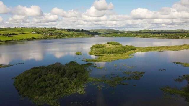 An aerial footage of green islands in the middle of river Lee during high tide and white clouds reflected on blue surface of water. County Cork, Ireland.
