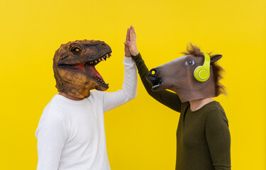 Excited couple of cheerful man and woman wearing dinosaur and horse head mask giving high...