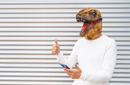 Happy man wearing dinosaur mask using smart phone showing thumb up