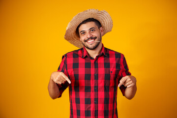 man dressed in junina party clothes with his fingers indicating that it is here, indicating the...