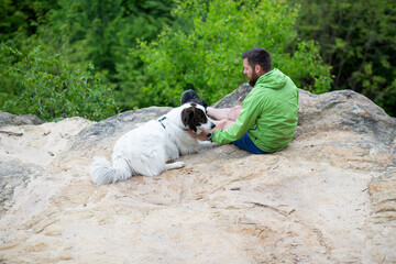 Fototapeta premium man with his dog sitting on a rock enjoying nature
