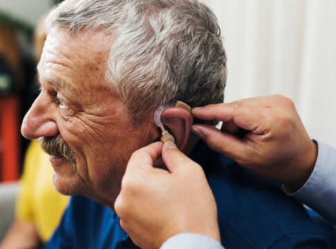 Doctor inserting hearing aid to patient's ear