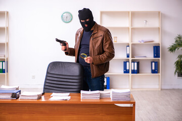 Young man in balaclava stealing information from the office