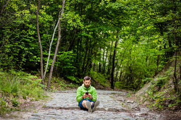 man sitting in green forest looking at phone