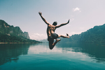 Man jumping with joy by a lake - Powered by Adobe