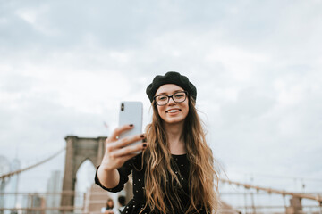 Cheerful woman taking a selfie with The Brooklyn Bridge, USA