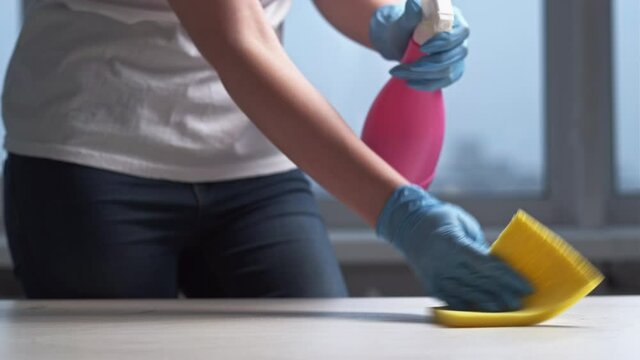 Furniture cleaning. Detergent product. Careful room hygiene. Unrecognizable woman protective gloves using spray for washing table surface with soapy sponge wiper light home interior.
