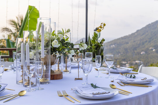 Romantic Wedding Table Top Layout Table Spread no people tropical location with gold cutlery white table cloth and scenic view of sunset with copy space tablescape, beautiful paradise setting