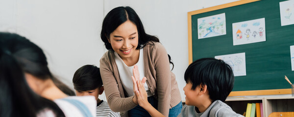 Young Asian teacher giving boy high five in school, success, achievement, happiness. Asia school boy with young woman in class. - 436772787