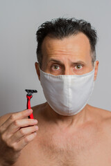 Close up of a surprised man shaving with a razor wearing a protective mask, looking at camera surprised, isolated on a white background. Vertical, pandemic, coronavirus.