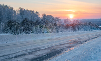 winter, frosty morning landscape of the rising sun with sun glare on the background of a slippery,...