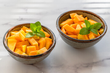 Cantaloupe melon bite-sized cubes close up in a bowls on light marble background. Fruit salad,...