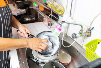 A housewife is washing the pan at the sink.
