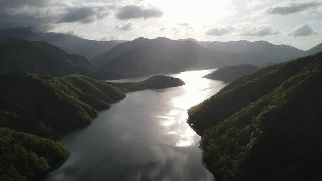 岐阜県の徳山ダム。山のシルエットとダムの湖面に反射する太陽。