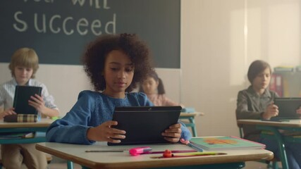 Smiling african american girl using digital tablet in class with classmates  - Powered by Adobe