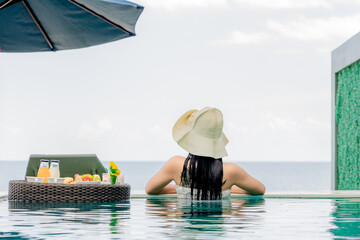 Happy woman in white swimsuit swimming in luxury pool hotel, young female with hat enjoy in tropical resort. Relaxing, summer travel, holiday, vacation and weekend concept