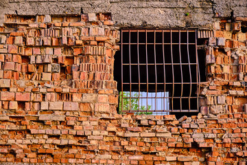 Metal grate in the brick wall of the destroyed house; blue sky through the barrier