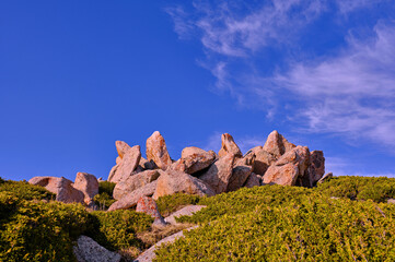 Exquisite rock formations among the juniper bushes on a background of blue sky with clouds