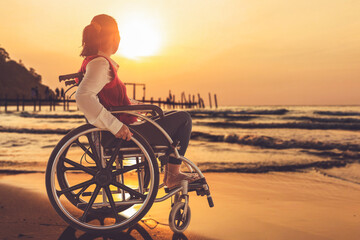 Disabled handicapped woman sitting on wheelchair at the beach sunset