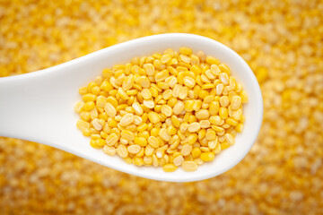 Macro Close up of Organic yellow Gram (Vigna radiata) or split yellow moong dal inside a ceramic white soup spoon in a blurred background. Top view