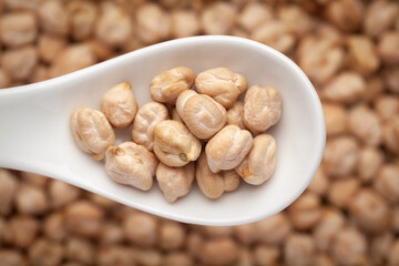 Macro Close-up of Organic chhole chana or Kabuli chana (Cicer arietinum) or whole white Bengal gram dal on a white ceramic soup spoon in a blurred background. Top view