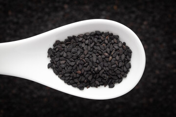 Macro Close up of Organic Black Sesame seeds(Sesamum indicum) or Black Til with the shell on a white ceramic soup spoon in a blurred background. Top view