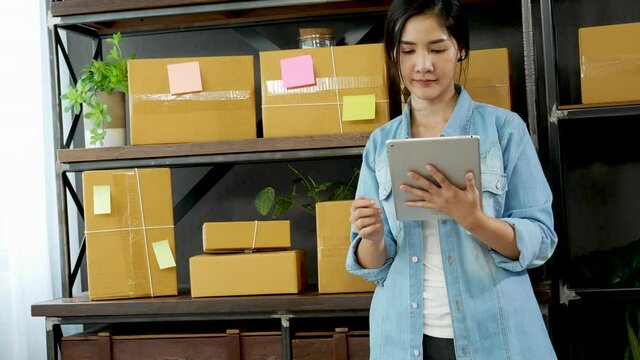 Asian woman startup small business at home office. Online seller entrepreneur young asian woman use tablet checking online order. Woman using tablet check stock goods supply delivery package shipping