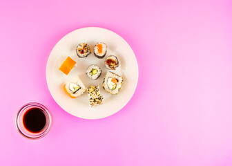 Composition of rolls on a white plate, soy sauce on a pink background. Asian food concept. View from above. Copy space