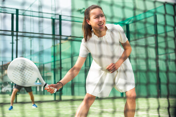 Portrait of smiling woman paddle tennis player during couple match at court, selective focus through net