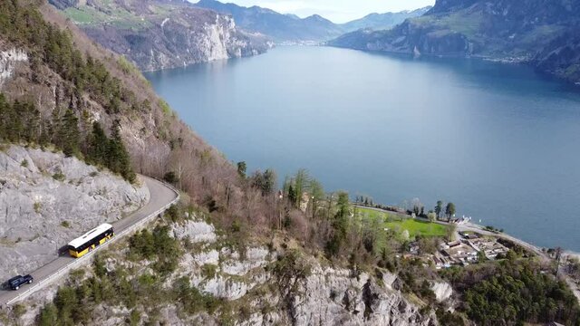 a typical yellow swiss post bus drives on a mountain road in front of the picturesque urnersee (lake uri)