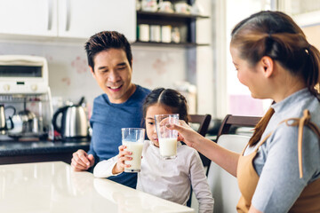 Portrait of enjoy happy love asian family father and mother with little asian girl smiling and having breakfast drinking and hold glasses of milk at table in kitchen