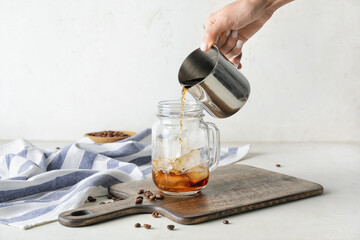 Pouring of cold brew coffee into mason jar on white background