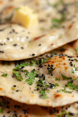 Close-up of fresh, hot tandoori roti or butter naan garnished with black till and green fresh coriander leaves. A typical, traditional north indian panjabi food.