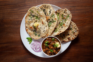 Close-up of fresh, hot tandoori roti or butter naan garnished with black till and green fresh coriander leaves and chole. A typical, traditional north indian panjabi food. - obrazy, fototapety, plakaty