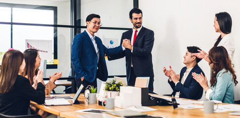 Image two asian business partners in elegant suit successful handshake together in front of group of casual business clapping hand in modern office.Partnership approval and thanks gesture concept