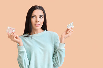 Thinking young woman with pills on color background