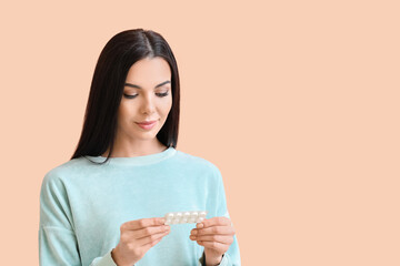 Beautiful young woman with pills on color background