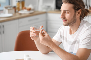 Handsome young man taking pills in kitchen - obrazy, fototapety, plakaty