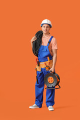 Young electrician with cables on color background